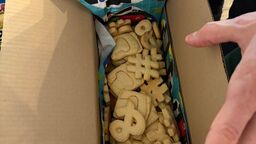 An open box inside the care package contains homemade cookies shaped like special characters and Contao motifs.